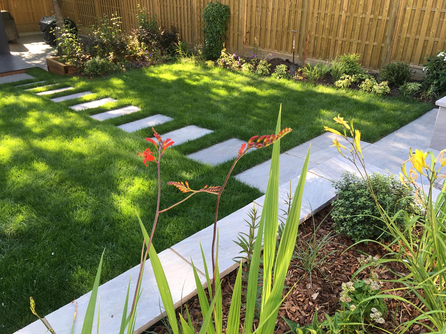 Riven grey sandstone, raised retaining beds, create a space for planting. The grasses help to screen the garden without disrupting the view.