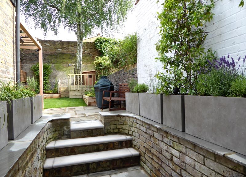 Bullnosed steps, an off-white wall and terrazzo planters containing shade-tolerant plants make for a grand entrance from the lower terrace.