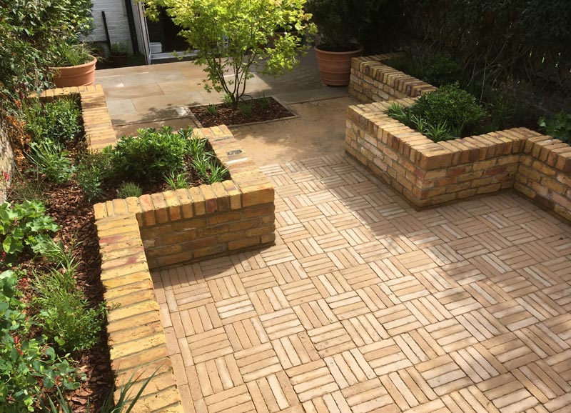 This landscape design for a courtyard garden in Barnsbury, London N1, features a sandstone patio near the house, an entertaining area with clay pavers, and lighting at night.