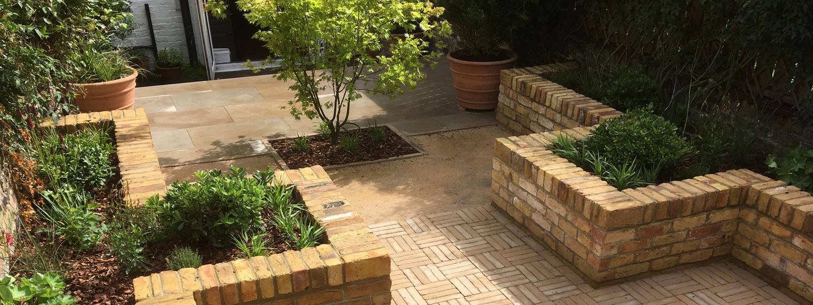 This landscape design for a courtyard garden in Barnsbury, London N1, features a sandstone patio near the house, an entertaining area with clay pavers, and lighting at night.
