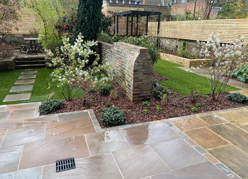 With low-maintenance shrubs, natural materials, sandstone paving, larch screening and complementary brickwork, two spaces work independently or as one larger area for relaxation and entertainment.