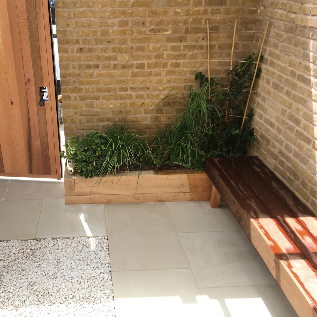 The low maintenance evergreen planting, grey sandstone paving, Cotswold stone gravel, Hardwood bench and minimalist design makes this small garden feel light and spacious.