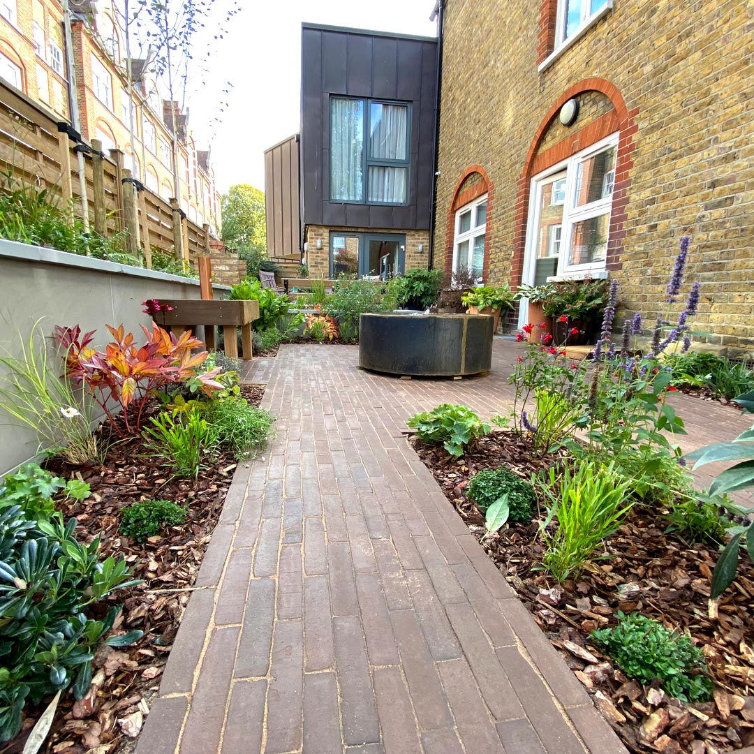 Looking towards the house the corten steel water table relates back to the modern zinc clad extension, the clay pavers picking out the reds of the original brickwork.