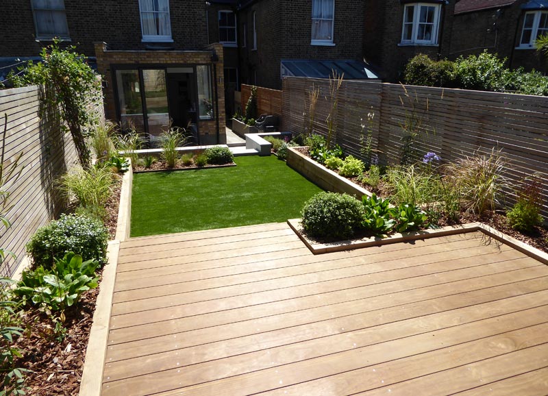 View of the garden looking across from the raised decking area, across the lawn, to the dining/seating area on the patio to the rear of the house.