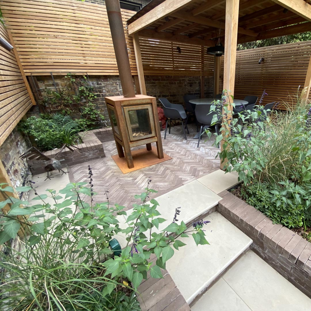 Raised patio for outdoor living and entertaining. Clay pavers laid in a Herringbone pattern, framed with grey sandstone paving.