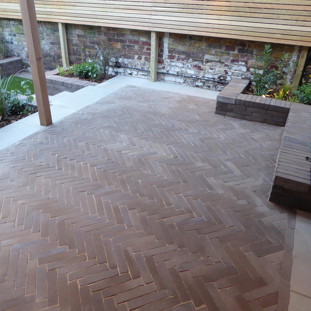 A detailed view of the Vande Moortel Sepia clay paver patio laid in a herringbone pattern.