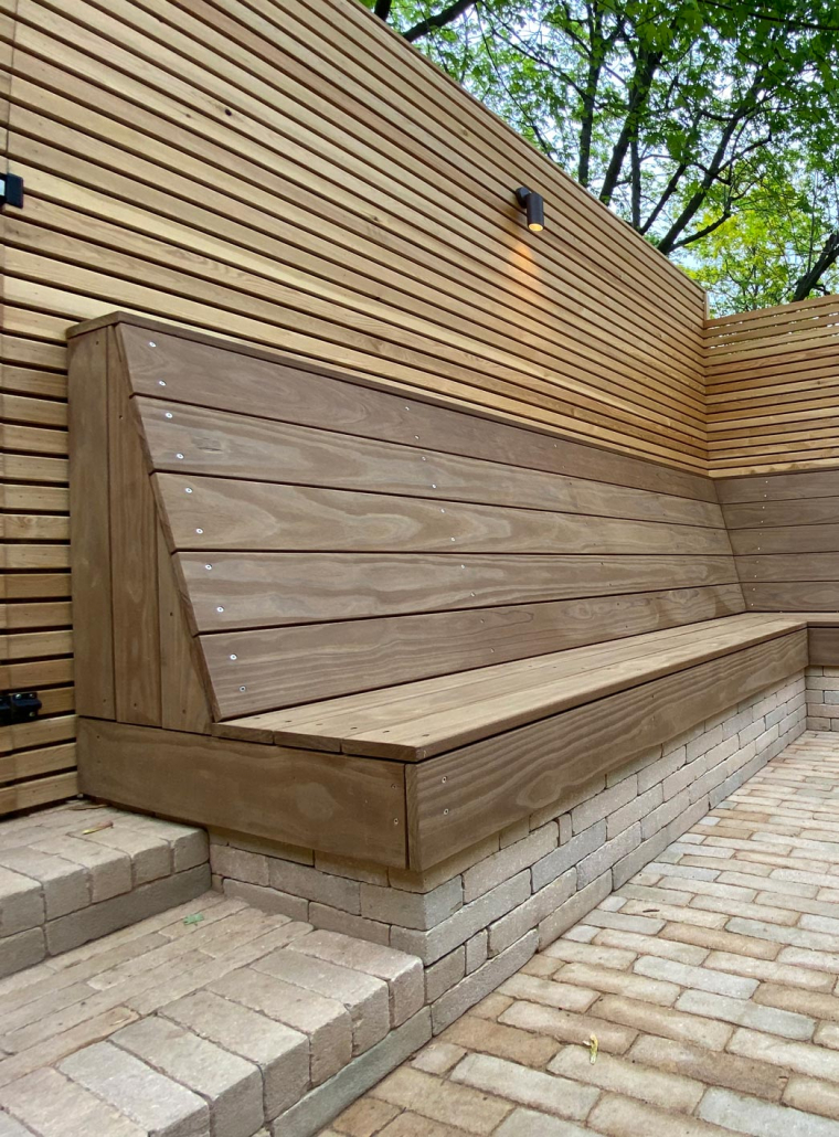 A space saving L-shaped bench on a clay paver brick plinth with a slanted high back.