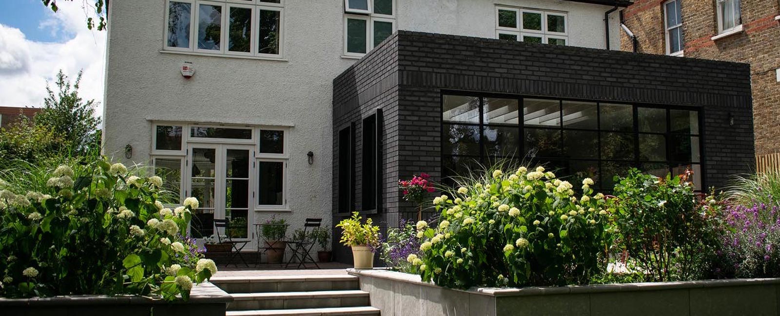 Here you can see the side terrace to the left of the new extension, new steps, raised flower beds, and the herbaceous planting in an English style with some Mediterranean influences.