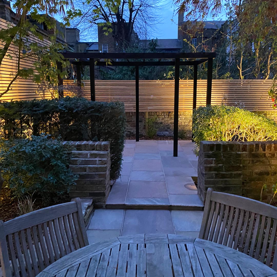 Looking across the interlinking back patios towards the simple pergola structure and bespoke larch fencing.