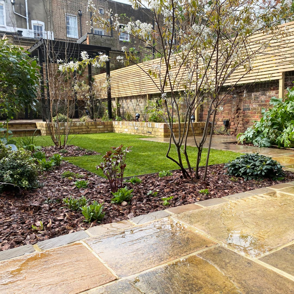 A view across this Islington garden shows some of the structural hardscape elements such as; sandstone paving, setts, yellow-stock brick retaining beds and a softwood pergola structure.