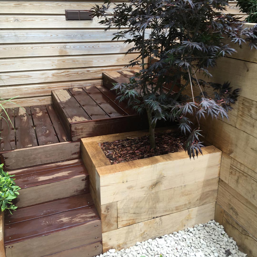 Hardwood steps wind their way down from the top terrace. A beautiful Acer palmatum ‘Bloodgood’ in a raised retaining oak sleeper bed greets you at the lower level.
