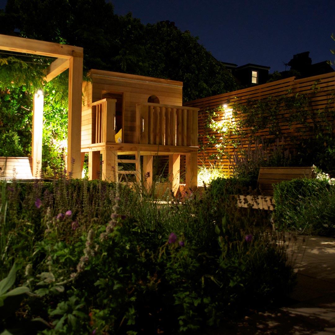 Warm background-lighting enhances the atmosphere of this mediterranean inspired planting design.