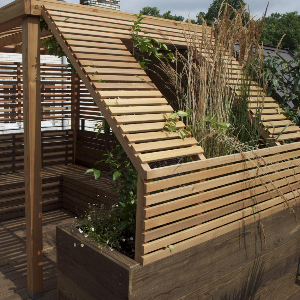 A rooftop pergola was designed to feature integral seating and bespoke wooden planters atop high quality screwless decking.